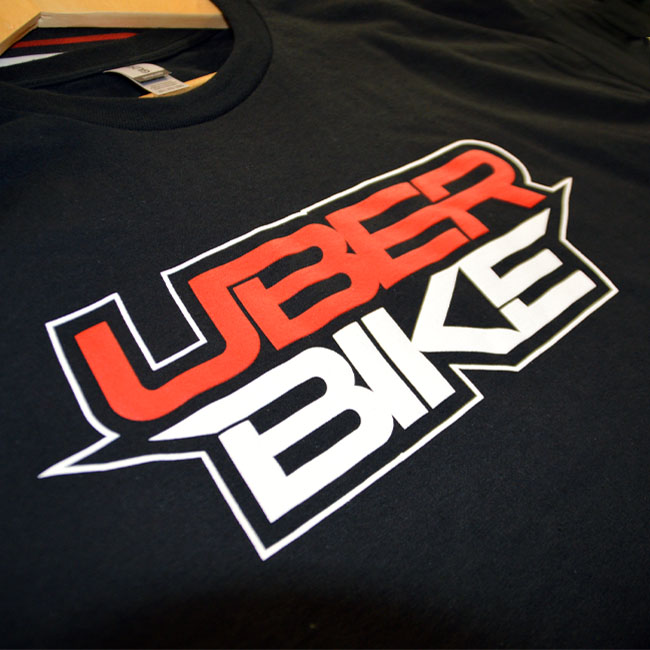 A close up of a black t shirt with the Uberbike stacked logo on 